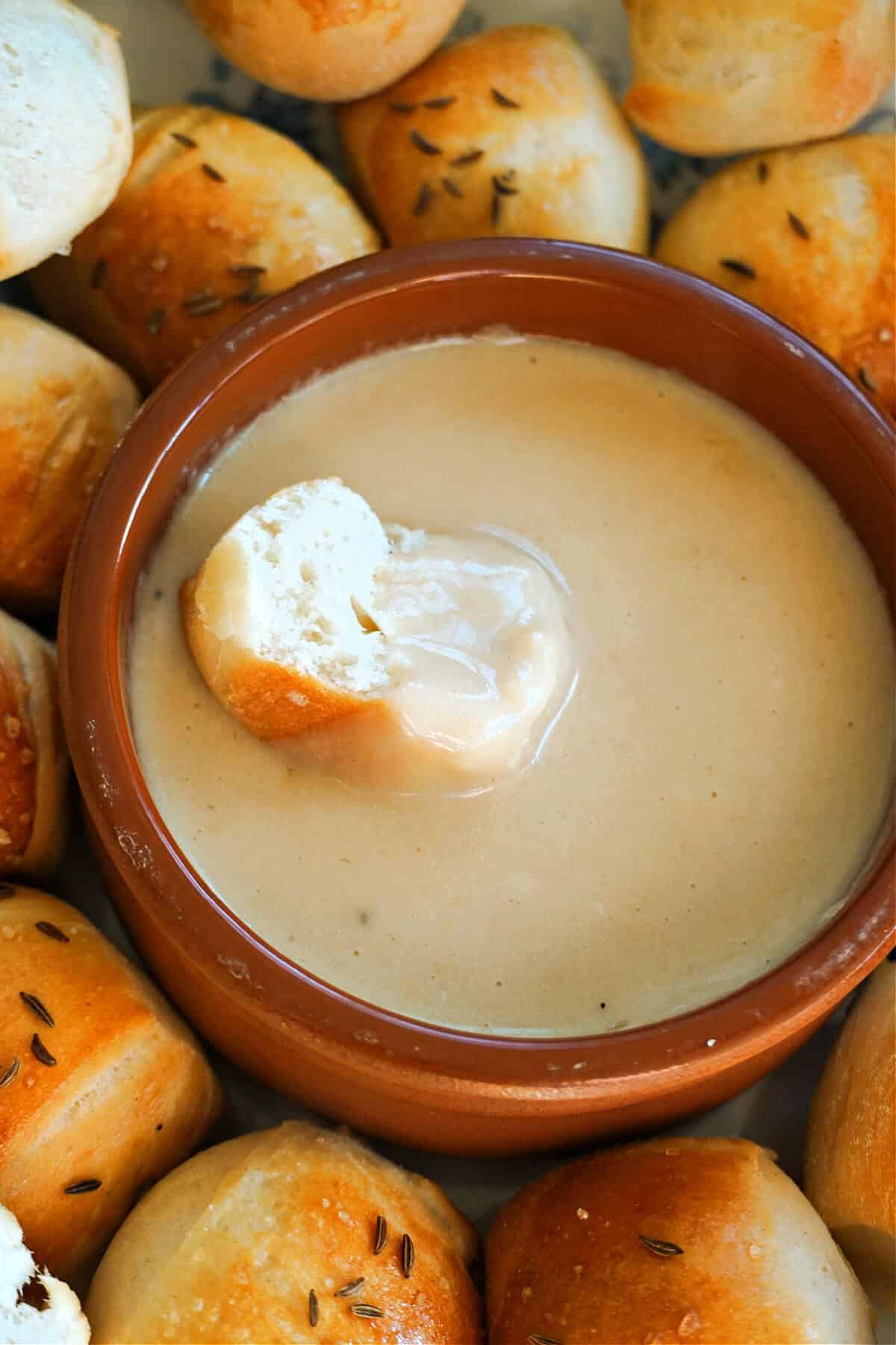 A ramekin with beer cheese dip and a half pretzel bite dunk into it.