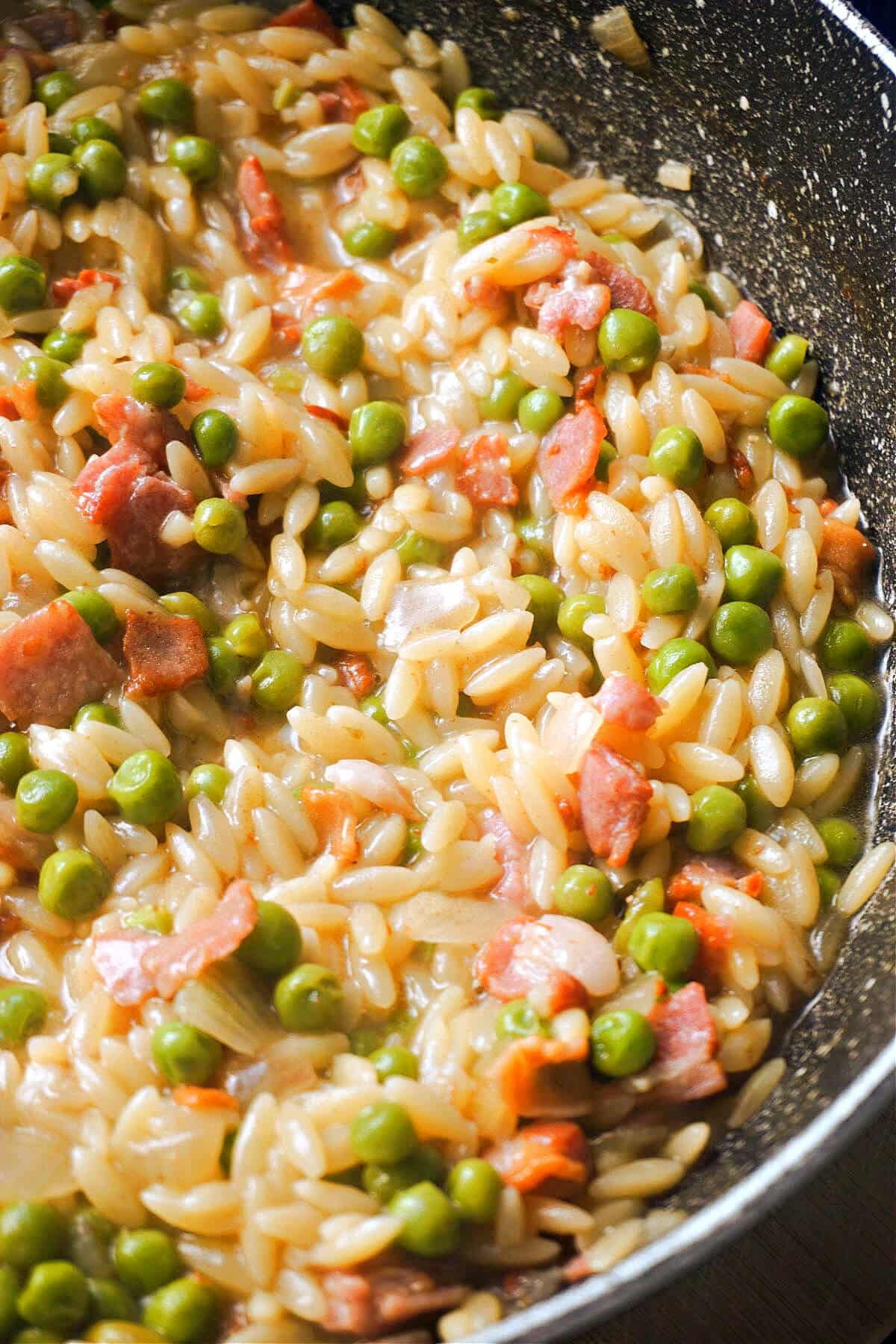 A pot with orzo with peas and bacon.