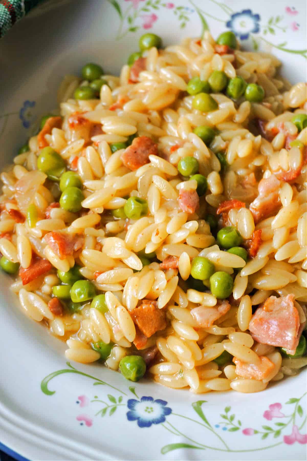 Close-up shoot of a plate of orzo with peas and bacon.