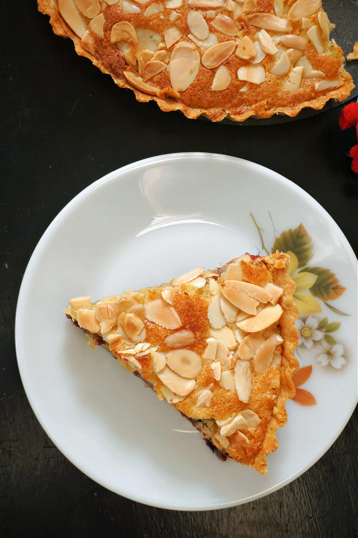 A slice of cherry bakewell on a white flowery plate.