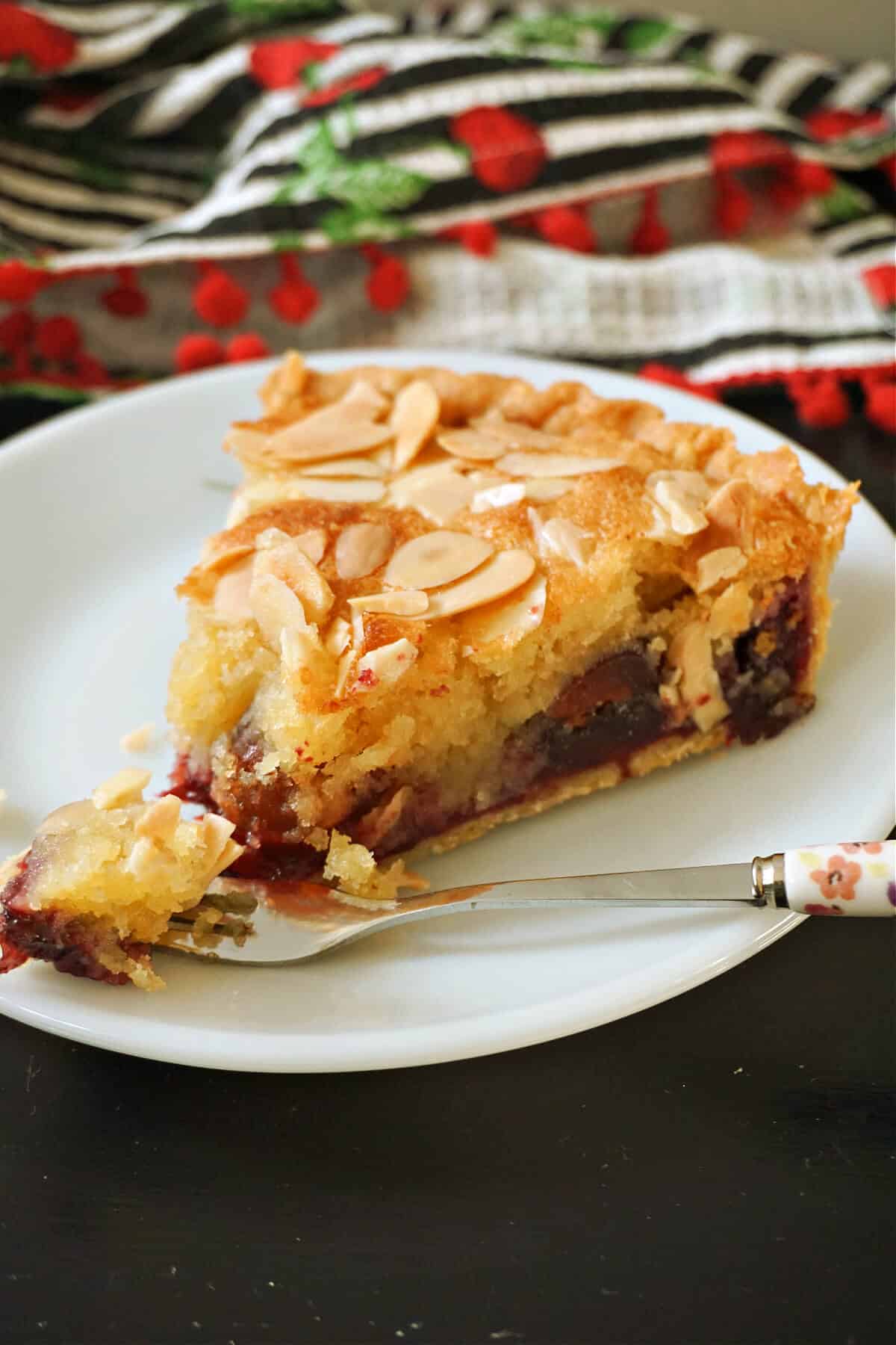 A slice of cherry bakewell tart on a plate with a fork on it.