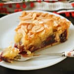 A slice of cherry bakewell tart on a white plate with a fork on it.