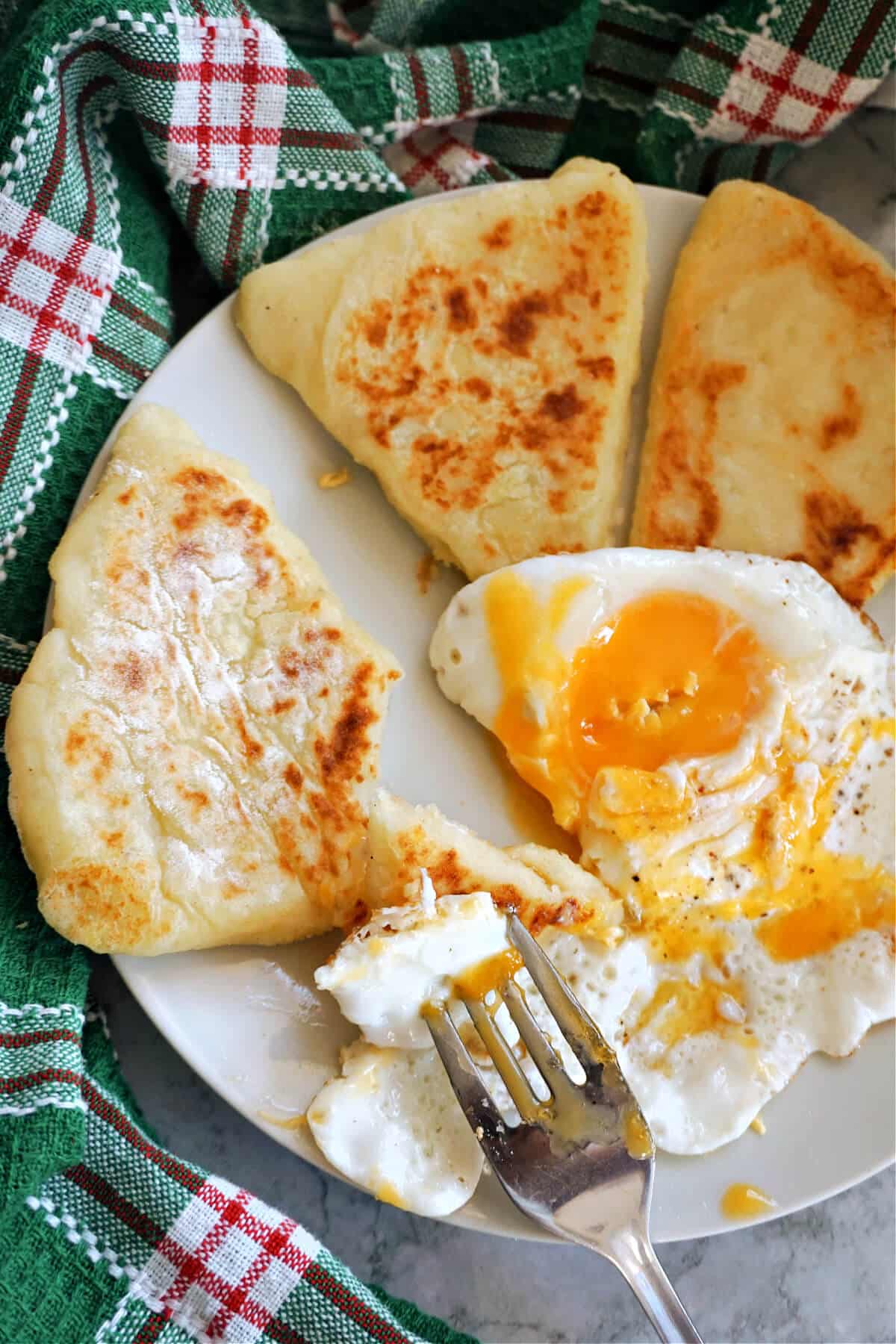 A plate with 3 potato cakes and a fried egg with a fork on it.