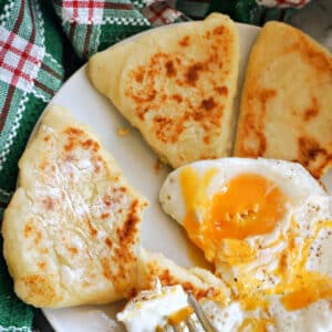 3 potato cakes with a fried egg and a fork on a white plate.