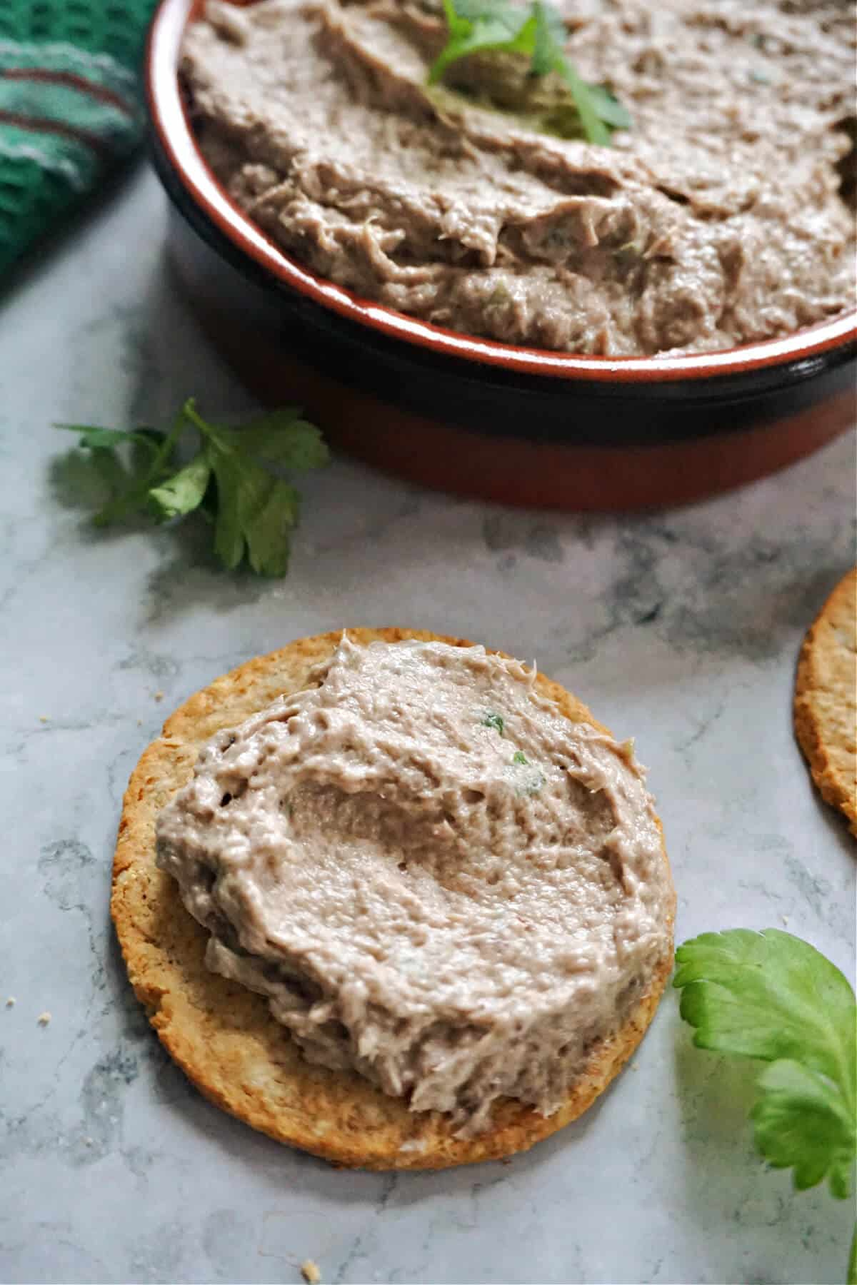 A cracker with sardine pate on it and a ramekin with more pate.