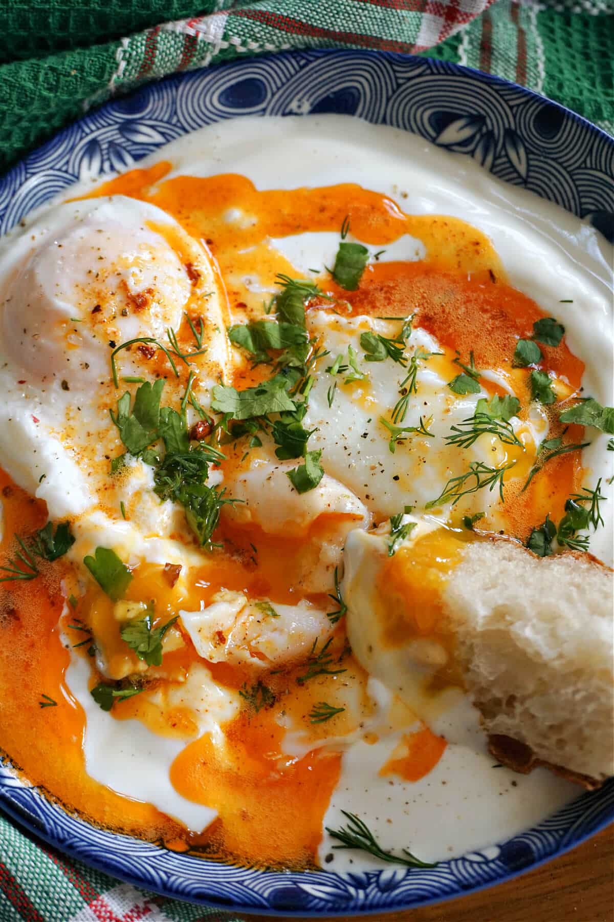 Close-up shoot of a blue plate with Turkish eggs and crusty bread scooping out the yogurt.