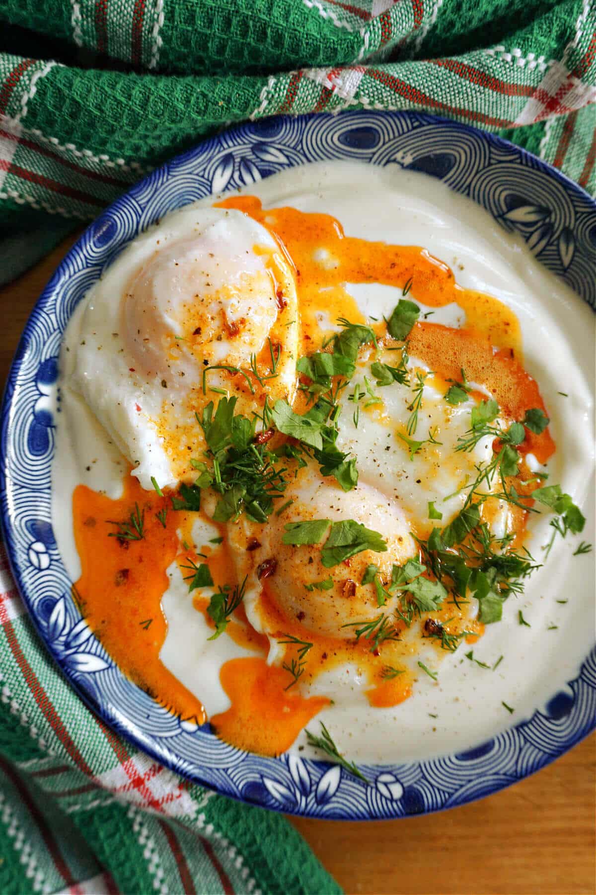 A blue plate with poached egg on a bed of yogurt, spicy sauce and chopped herbs on top.