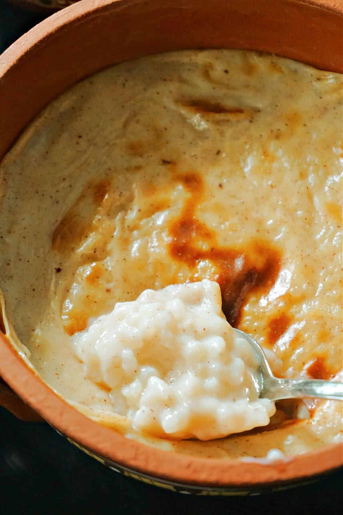 A clay pot of rice pudding with a spoonful of pudding.