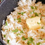 A pan with garlic rice garnished with fresh parsley and topped with a knob of butter.
