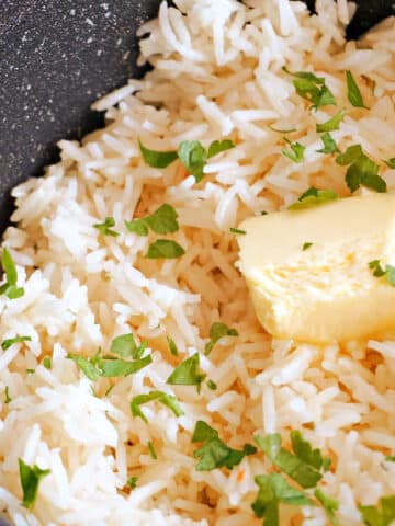 A pan with garlic rice garnished with fresh parsley and topped with a knob of butter.