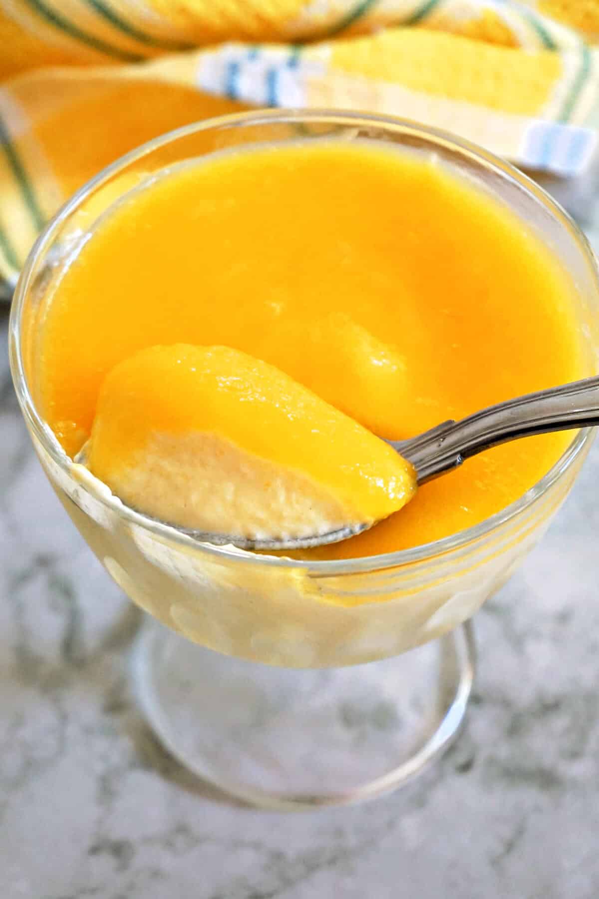 A glass with mango mousse and a spoonful of mousse.