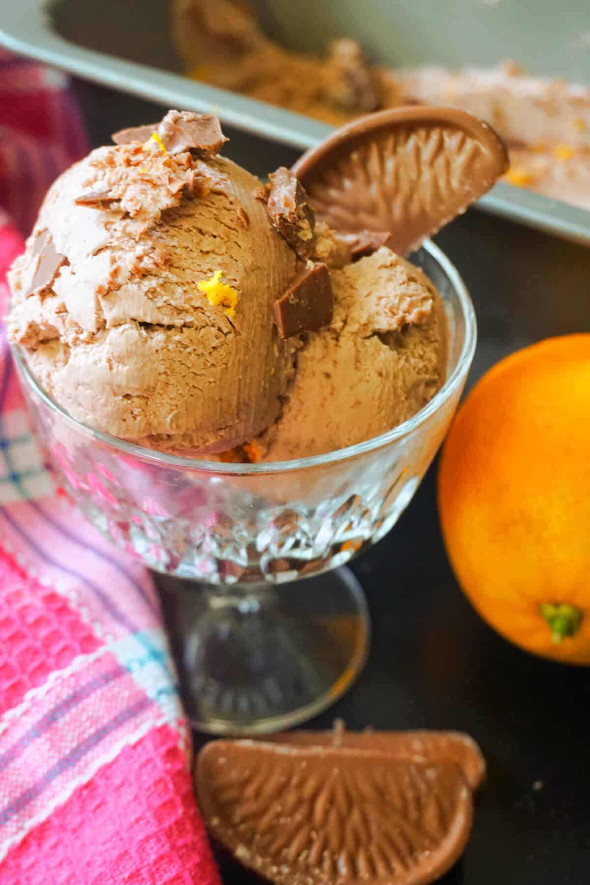 2 scoops of chocolate orange ice cream with a chocolate segment in a glass and an orange on the side.
