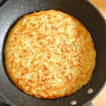 A potato rosti in a frying pan.