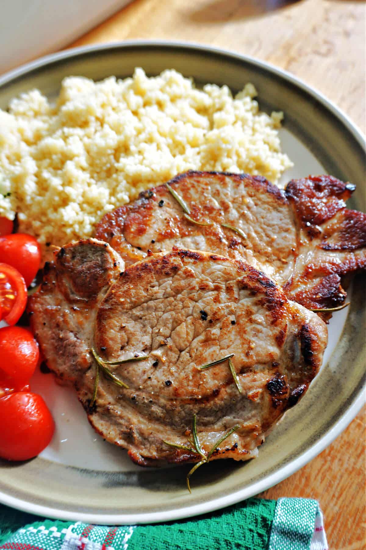 A pork steak with couscous and cherry tomatoes on a plate.