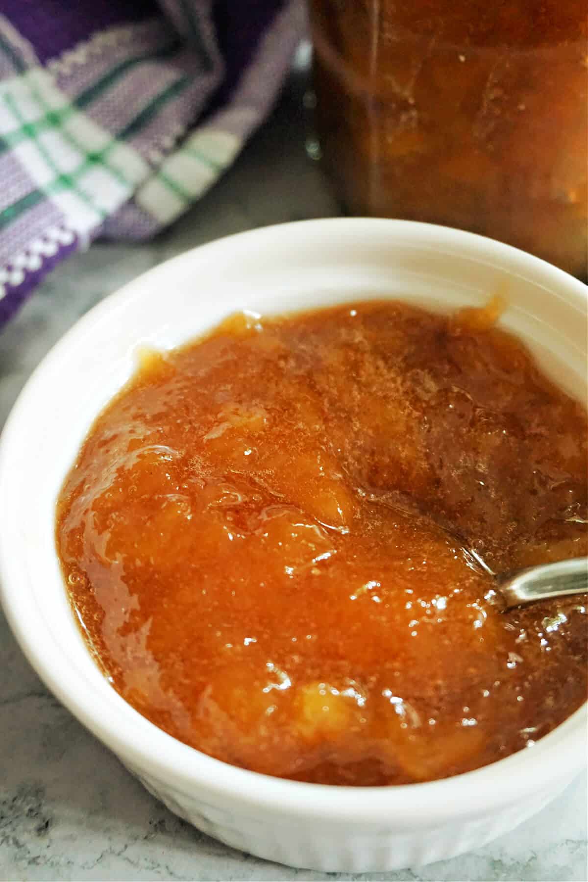 Peach jam in a white ramekin with a teaspoon in it.