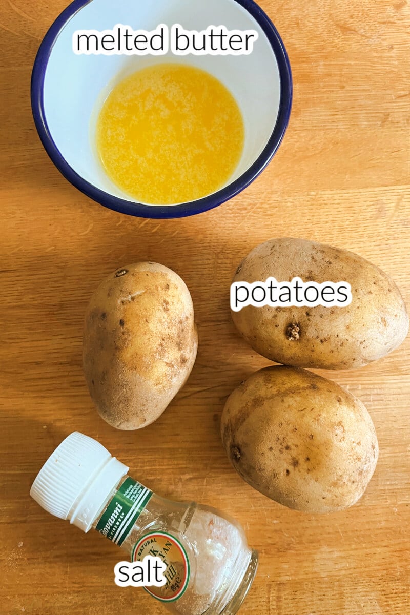 3 potatoes, a salt shaker and melted butter in a white ramekin.