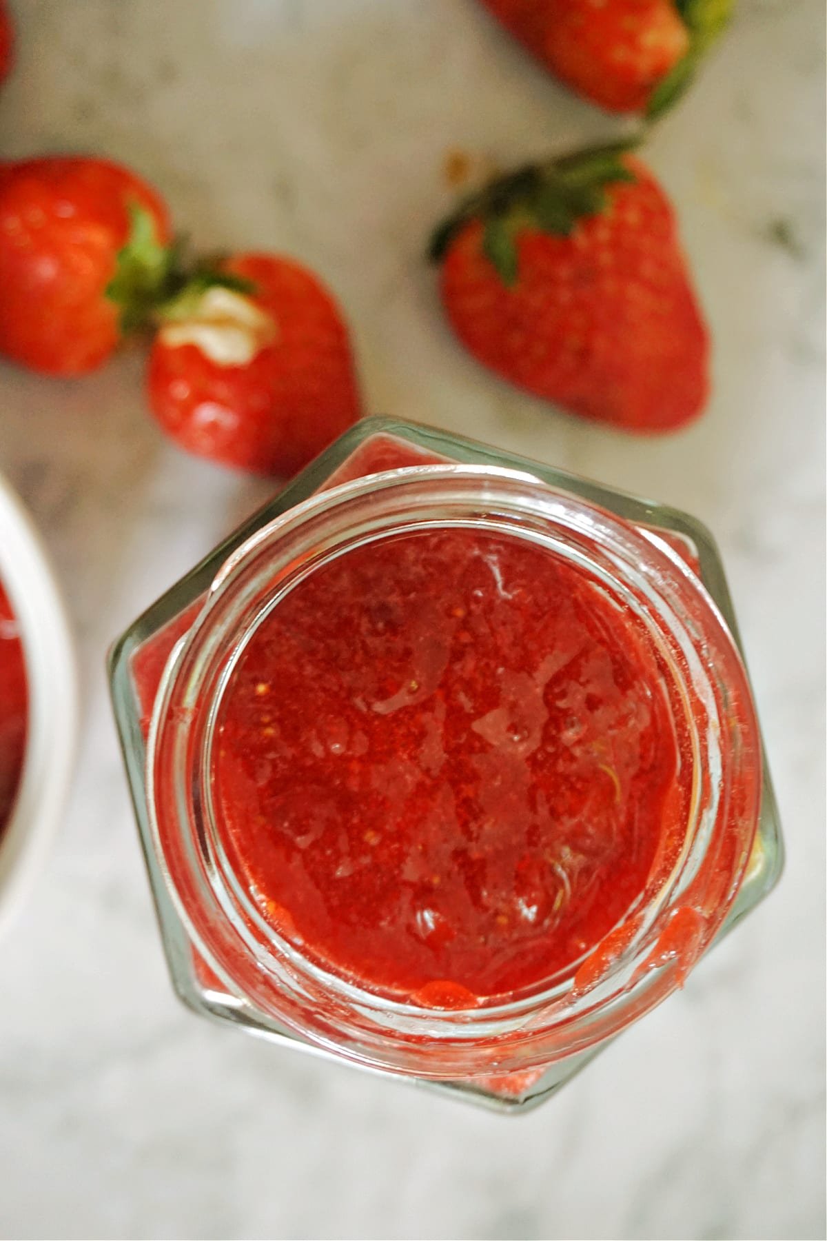 A jar of strawberry jam with 3 fresh strawberries around it.