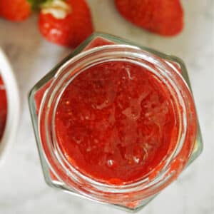 A small jar with strawberry jam and fresh strawberries around it.