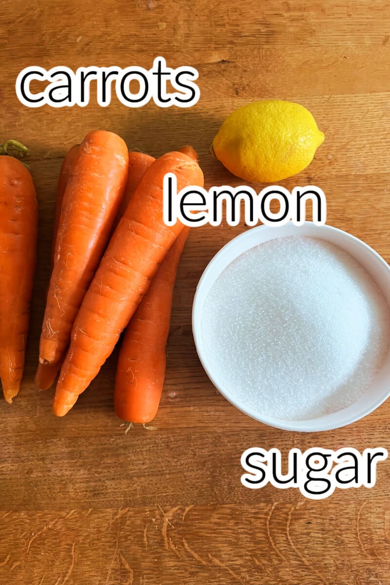 4 carrots, a lemon and a white ramekin with sugar on a table.