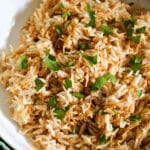 A white bowl with rice and vermicelli garnished with chopped parsley.