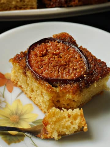 A slice of fig upside down cake with a dessert fork on a flowery plate.