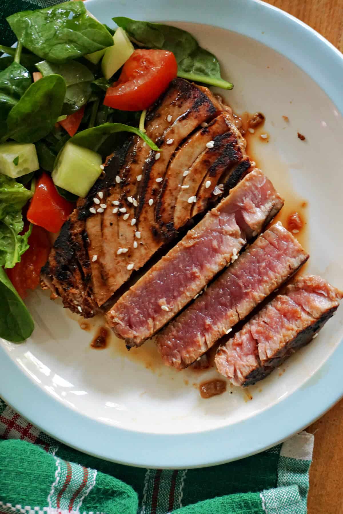 A sliced tuna steak with salad on a white plate.