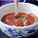 A white and blue bowl with fig jam and a teaspoon into it with a purple tea towel in the background