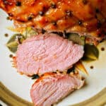 A plate with 2 slices of cooked ham and a whole ham next to them.