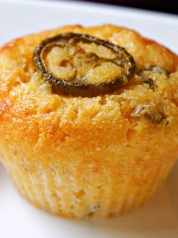 A cornbread muffin with a slice of jalapeno on top on a white plate.