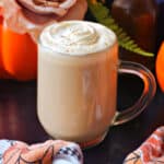 A glass of pumpkin spice latte on a black table with Autumn decorations around it.