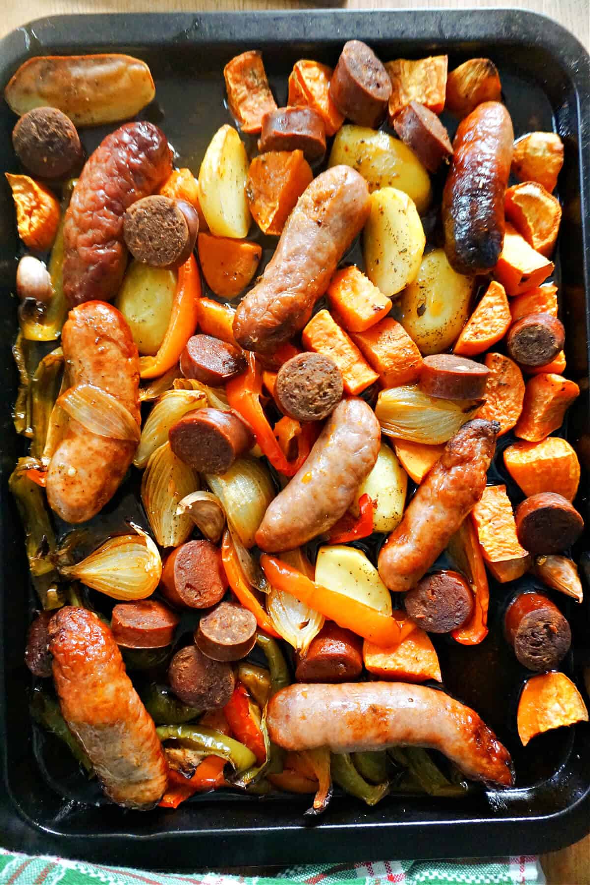 A tray bake with cooked sausages, chorizo slices and vegetables.