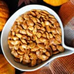 A white bowl with roasted pumpkin seeds and autumnal decorations around.
