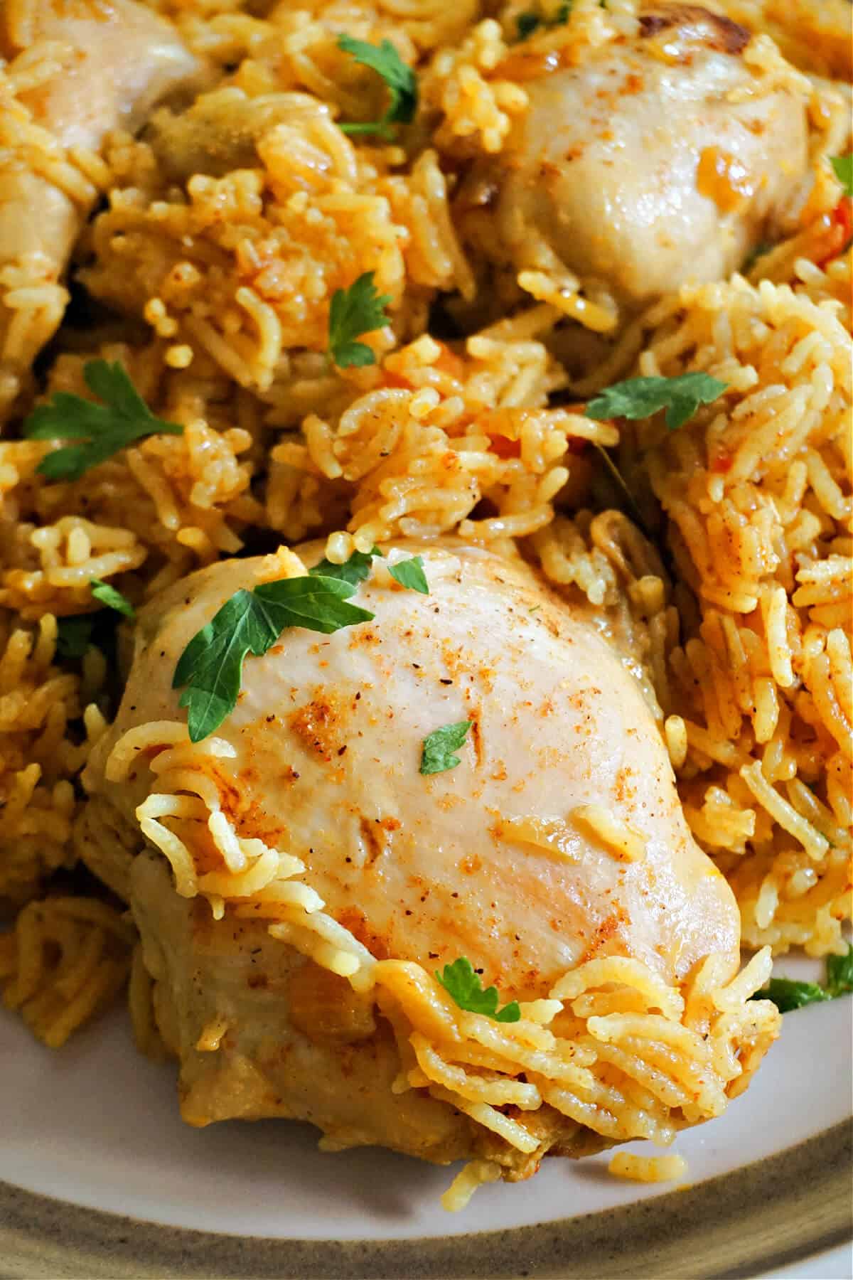 Close-up of a plate with chicken thighs and yellow rice garnished with chopped parsley.