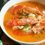 A white bowl with fish and prawn stew garnished with dill.