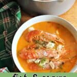 A white bowl of fish and prawn stew with a pot of stew and a green tea towel around them.