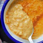 A white and blue ramekin with pumpkin rice pudding and a spoonful of pudding over the ramekin.