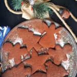 A plate with 8 cut-out chocolate gingerbread cookies , a festive decoration and a blue kitchen towel around the plate.