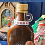 A bottle of gingerbread syrup with a gingerbead man cookie next to it and Christmas decorations around.