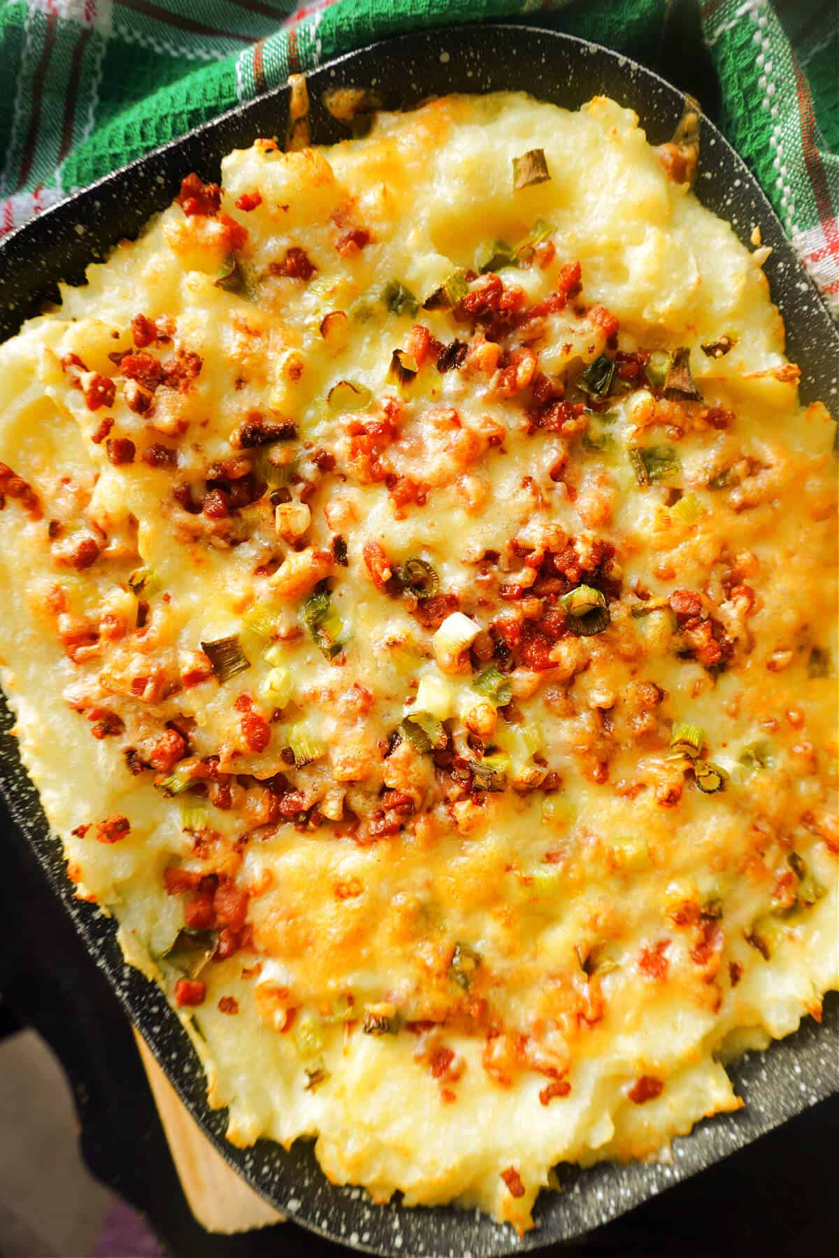 A casserole with loaded mashed potatoes and a green tea towel wrapped around the dish.
