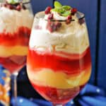 A glass with Christmas trifle and a partially glass with trifle behind it. A dark blur tea towel around the glasses.