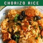 A plate with chicken and chorizo with rice garnished with chopped parsley.
