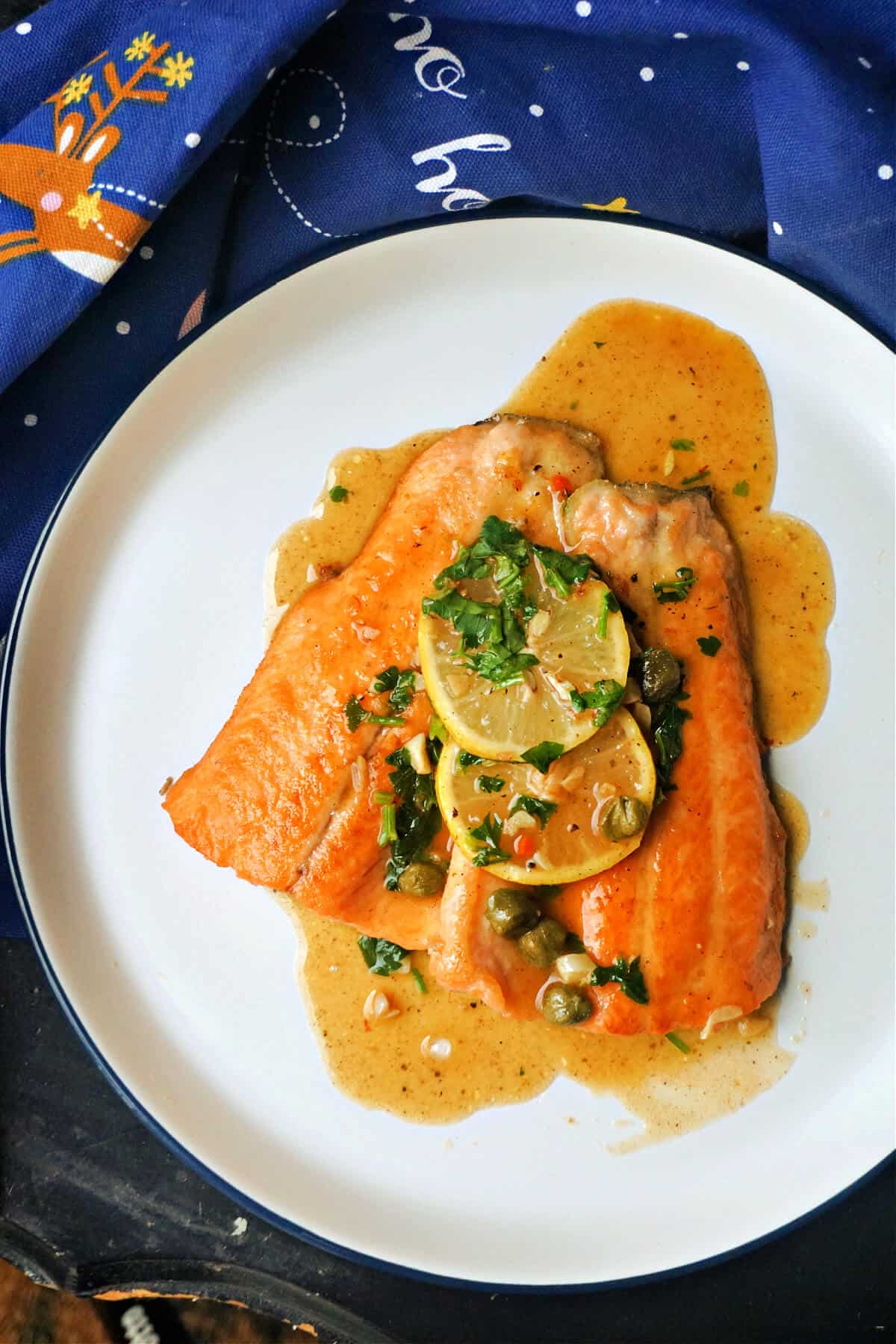 A plate with 2 fish fillets with 2 slices of lemon and sauce drizzled over.