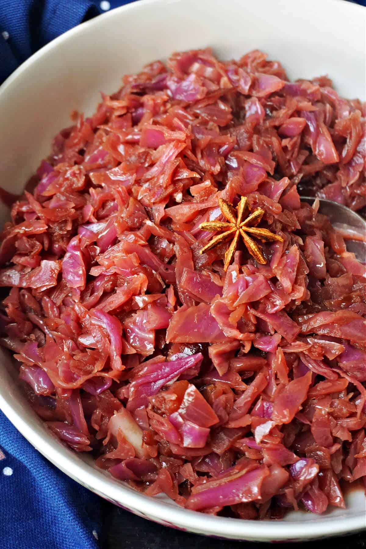 A white plate with braised red cabbage topped with a star anise.