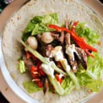 A plate with an open wrap with lettuce, shredded meat and veggies and mayo drizzled over.