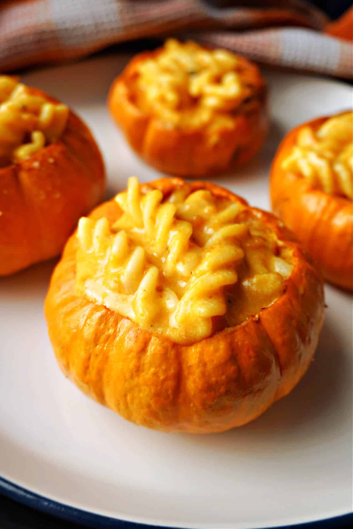A mini pumpkin stuffed with pumpkin mac and cheese and 3 other partially-visible mini stuffed pumpkins in the background.