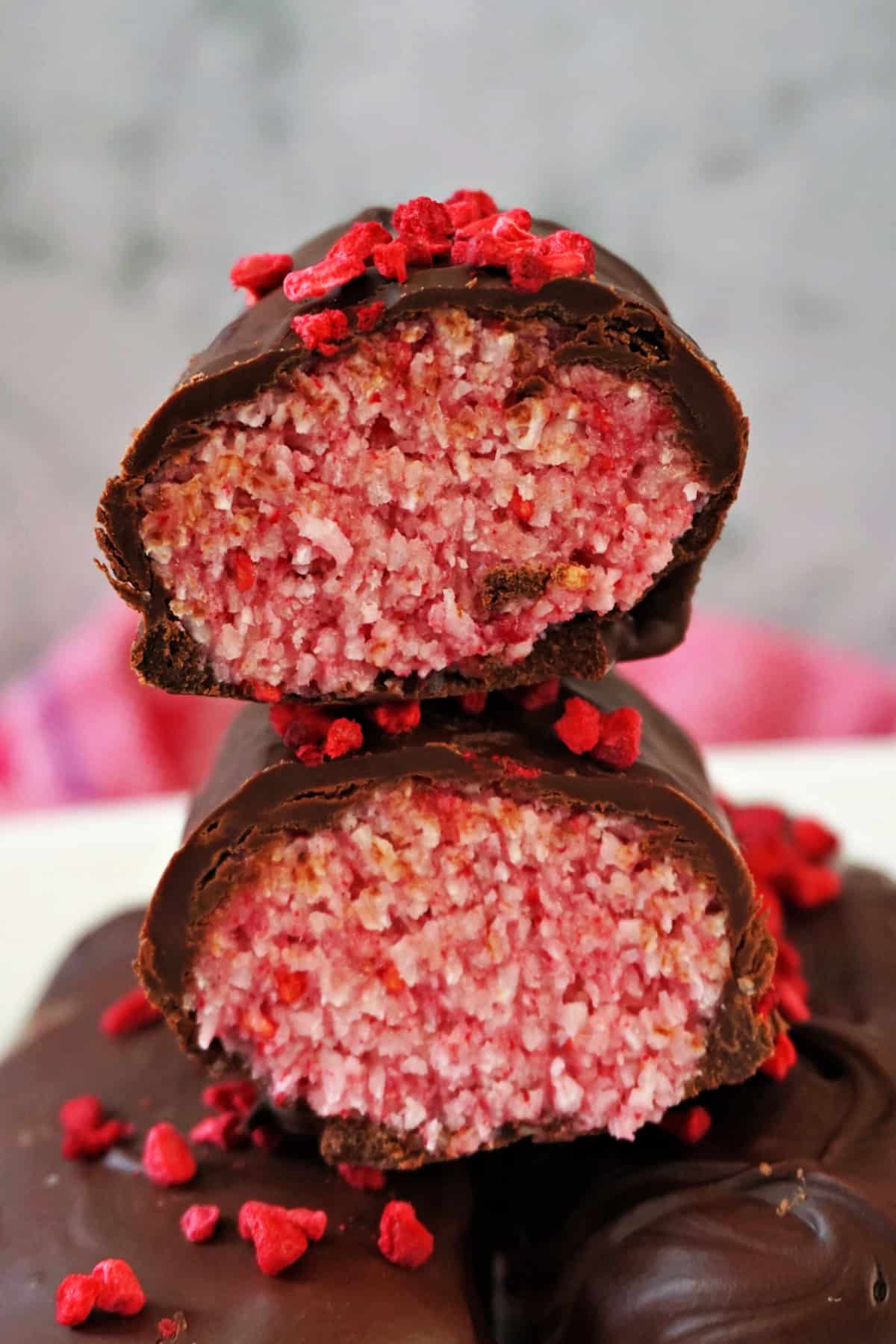 A stack of  2 halves of a raspberry coconut bar on top oh partially visible chocolate bars. 
