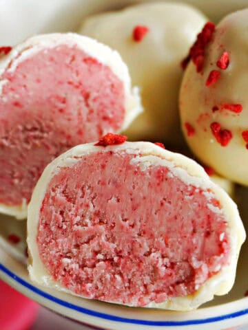 A small bowl with 2 halves of a raspberry white chocolate truffle and 2 whole truffles topped with red pieces.