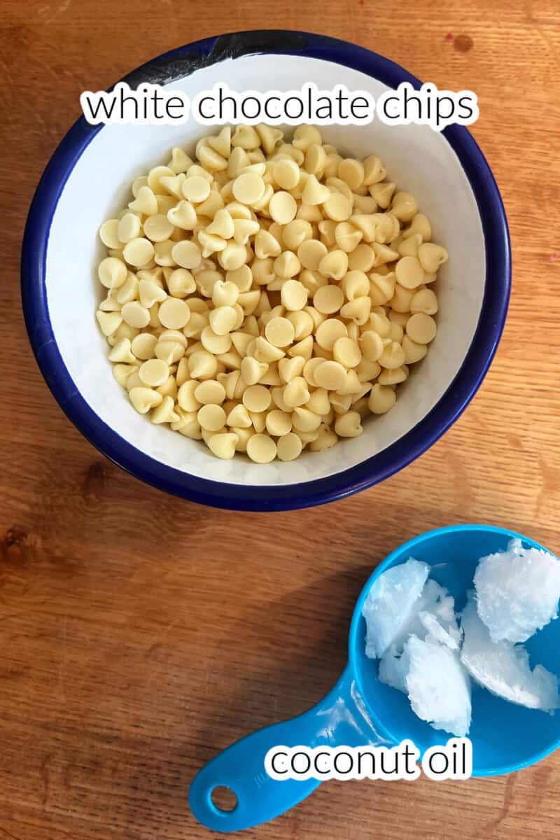A small bowl with white chocolate chips and a blue baking cup with coconut oil on a wooden table.