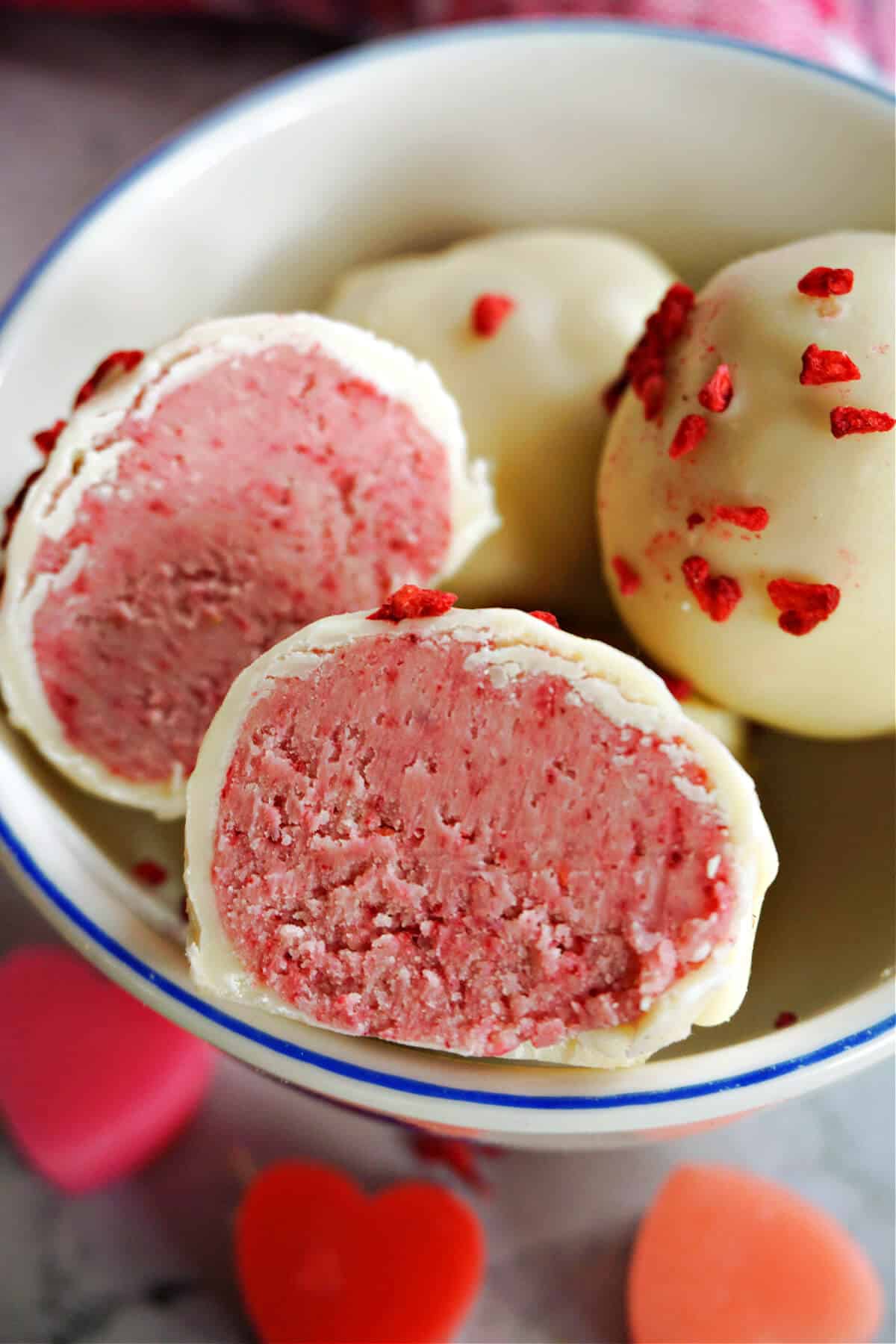 A small bowl with 2 halves of raspberry white chocolate truffles with other 2 whole truffles behind them.