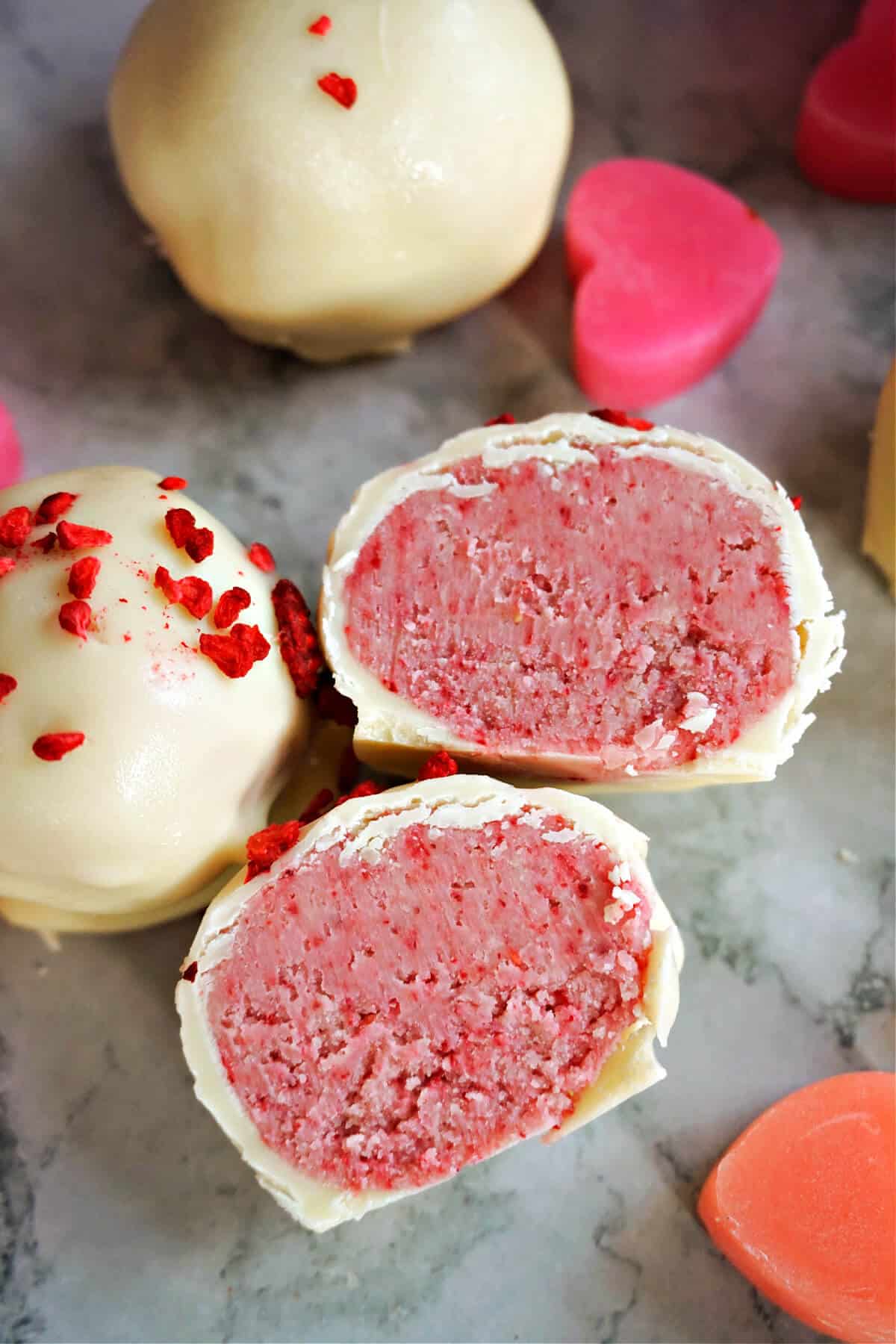 2 halves of a raspberry white chocolate truffle, other whole truffles and small heart decorations around them.